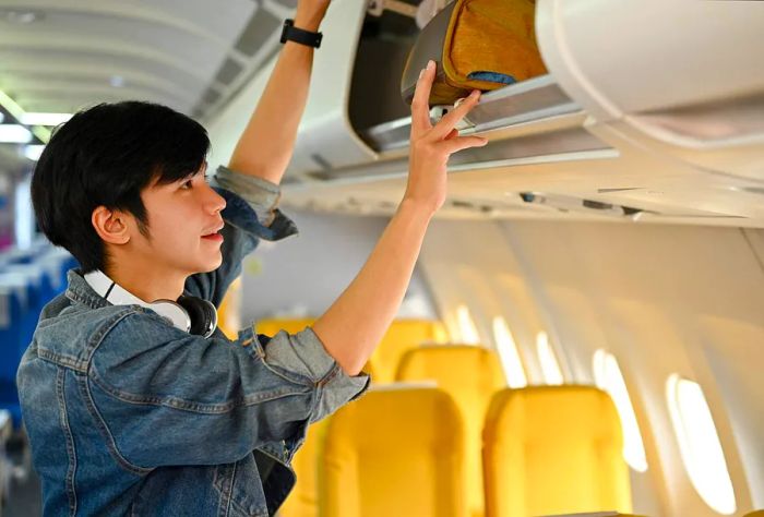 Man placing carry-on luggage in the overhead compartment on a plane