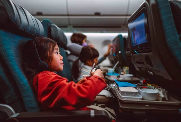 Child on an airplane enjoying a movie with a food tray