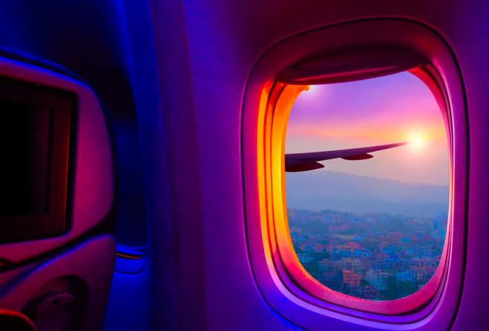 A stunning view from an airplane window featuring the sun setting behind mountains and colorful houses layered on the hillside.