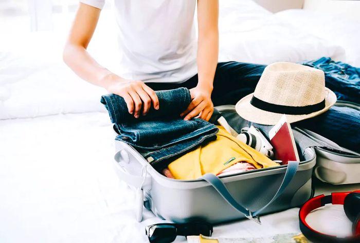 A woman organizing her suitcase with clothes, a hat, and other travel necessities.