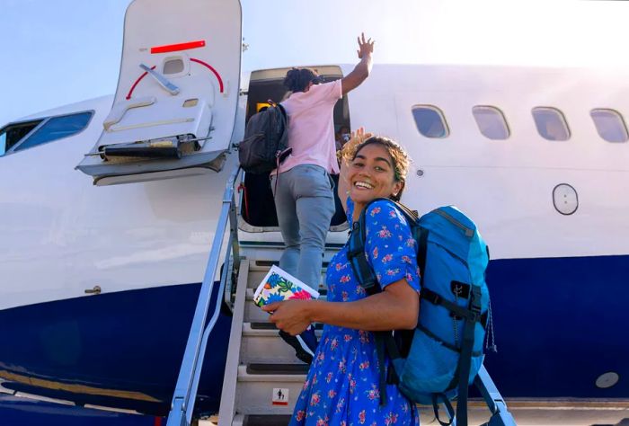 A picture of two young friends boarding a plane on the runway at the airport in Toulouse, France. One young woman glances over her shoulder with a smile at the camera, carrying a backpack and her boarding pass.