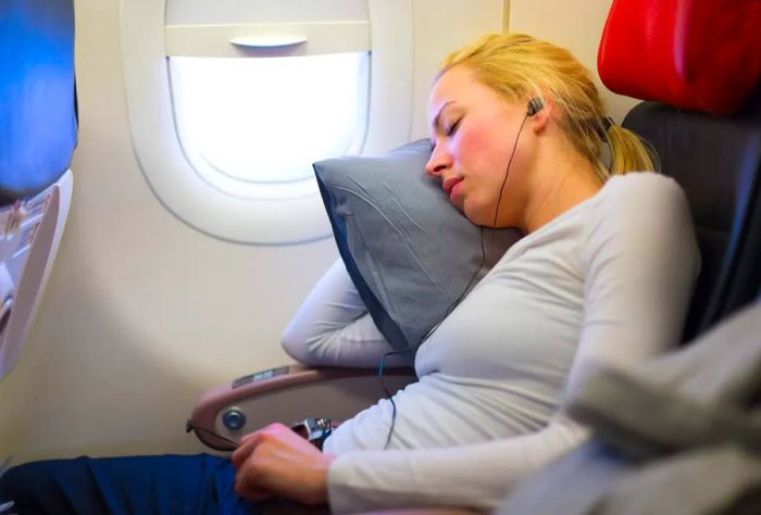 A blonde woman enjoys music while napping in her airplane seat.