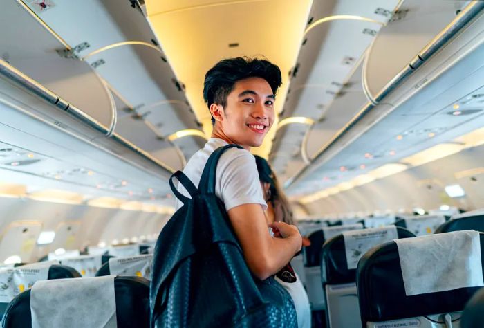 A young Asian male traveler boards a plane, carrying a backpack and looking back.