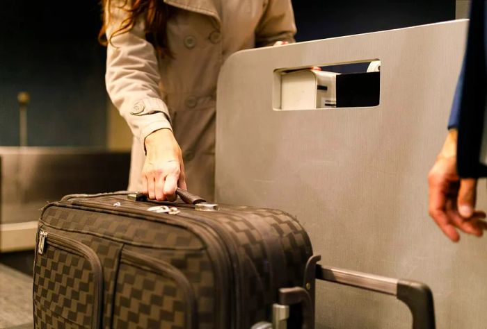 A woman weighs a brown checkered suitcase at a check-in counter.