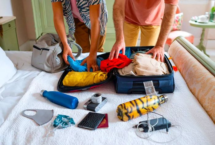 Two individuals organize their belongings on a bed as they prepare to pack a suitcase.