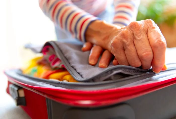 An individual zipping up one side of a suitcase.