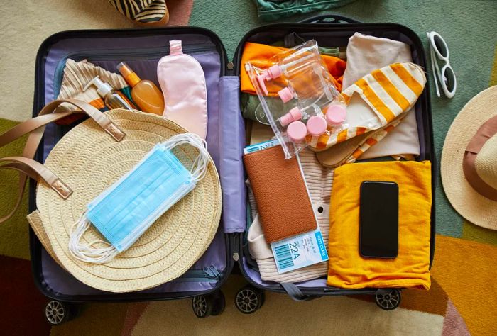 Luggage filled with vibrant travel essentials including face masks, reusable bottles, and a passport.