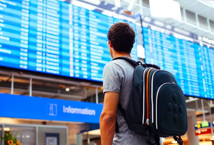 A man with a backpack checking the flight information display at the airport.