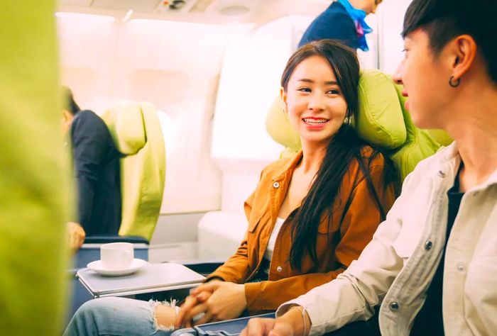 A young Asian couple shares a joyful conversation on an airplane, their faces glowing with happiness.