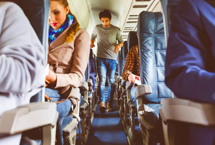 A man walks down the aisle of an airplane cabin, passing seated passengers.