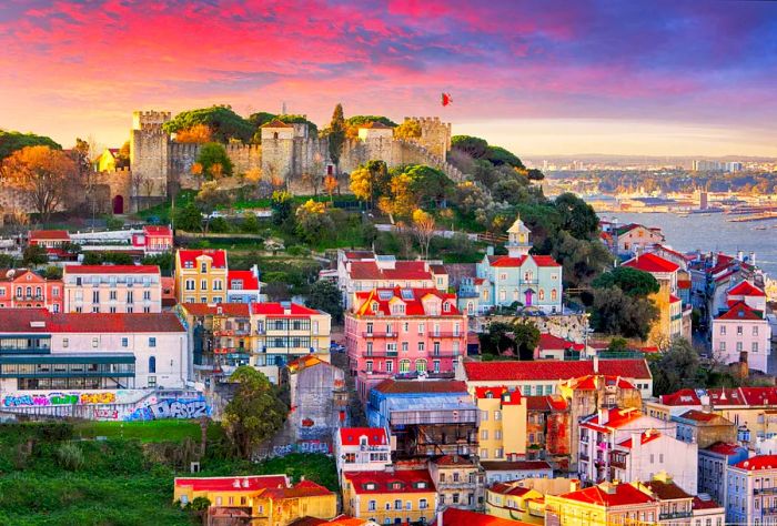 São Jorge Castle is a fortified structure sitting atop a wooded hill, surrounded by colorful buildings in a coastal city.