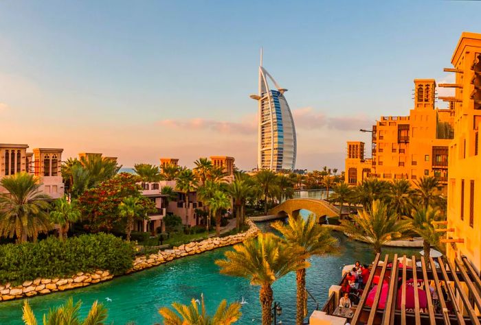 A picturesque water canal weaving through a neighborhood adorned with traditional Arab architecture and glimpses of the iconic Burj Al Arab in the distance.