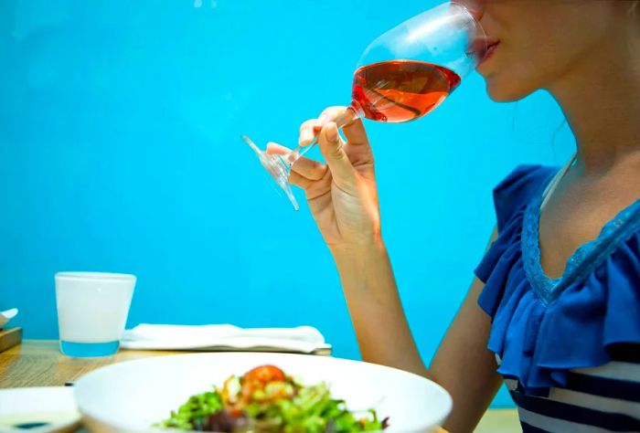 A person savoring a meal while sipping a glass of rosé wine.