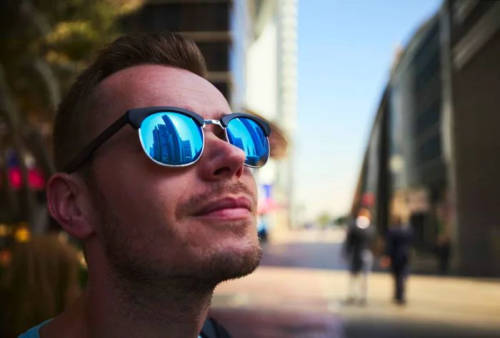 A man wearing sunglasses reflects the impressive skyline of towering skyscrapers.