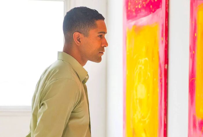 A man in a long-sleeve shirt gazes at abstract artwork on the wall.