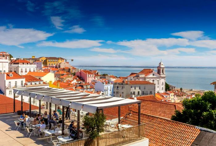 People enjoying a meal on a terrace with views over the city rooftops and the sea.