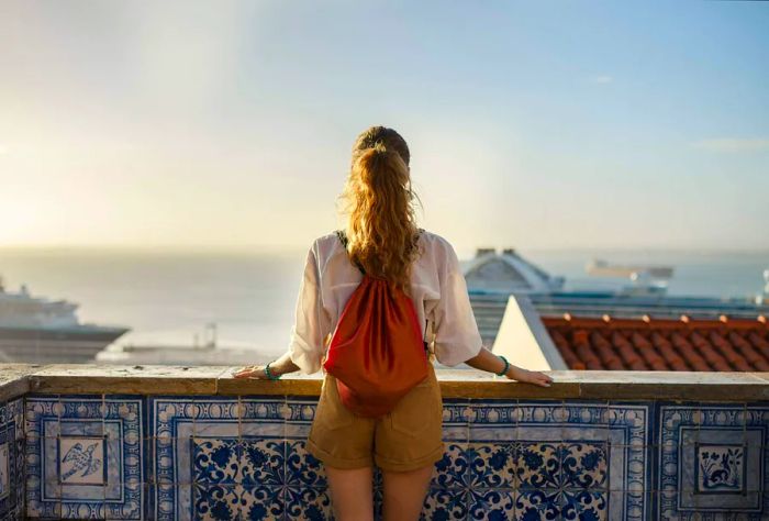 A woman on a rooftop gazing at the ships sailing in the sea.