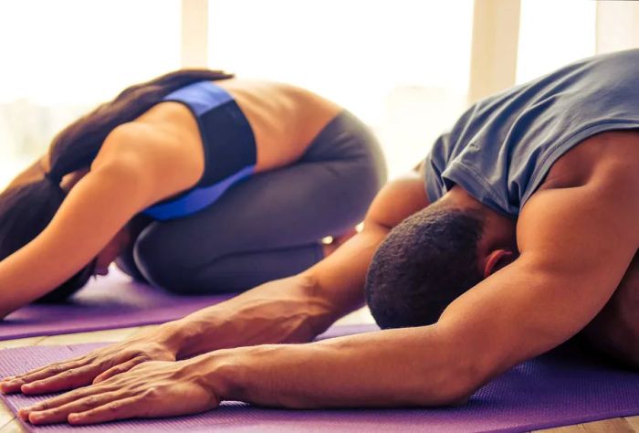 A lovely African American couple in athletic wear is stretching on yoga mats while exercising at home; Shutterstock ID 473389471; Purpose: Commercial emails; Brand (Dinogo, Momondo, Any): All; Client/Licensee: Carlee Shults