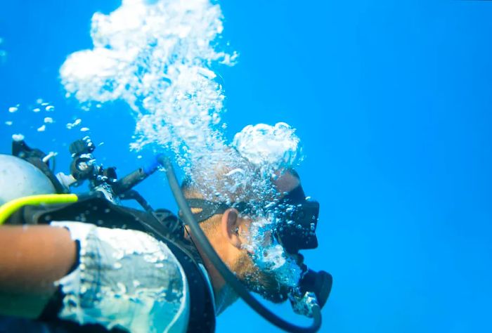 A scuba diver glides through the deep, crystal-clear turquoise waters, creating bubbles as they swim.