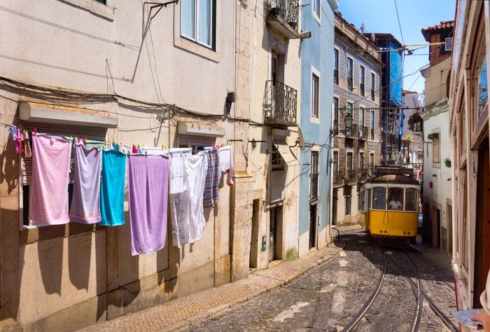 A classic tram travels down a narrow street adorned with traditional houses and clothes hanging out to dry.