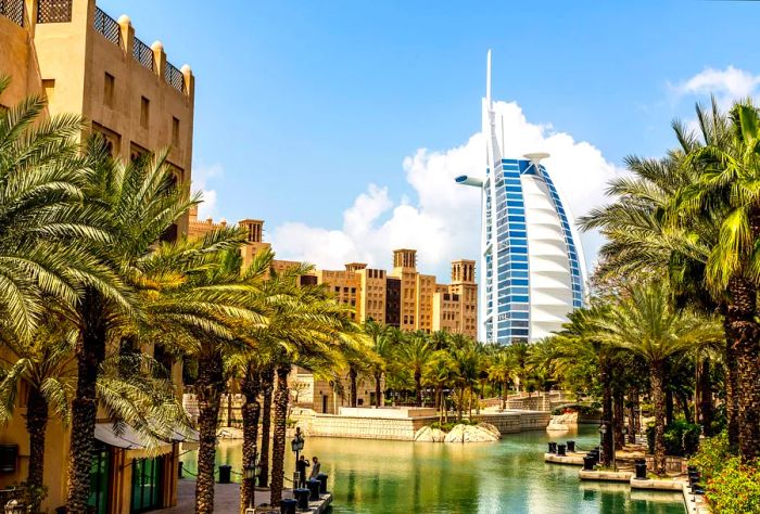 A picturesque park lake surrounded by palm trees, with the iconic Burj Al Arab in the background.