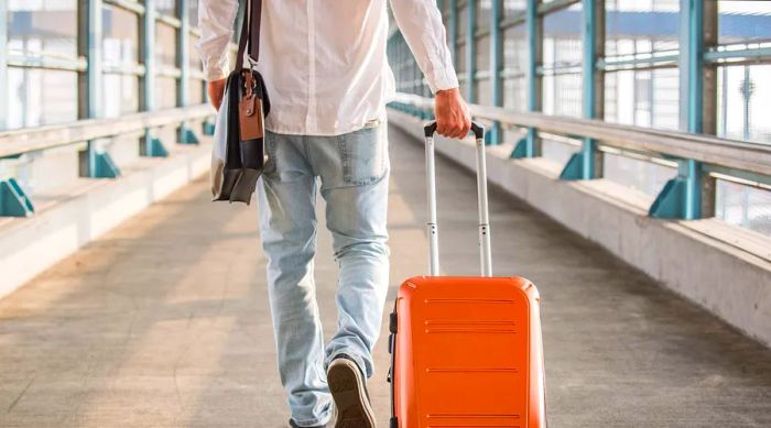 A casual-dressed man is seen walking toward a train station, carrying a backpack and pulling a suitcase behind him.