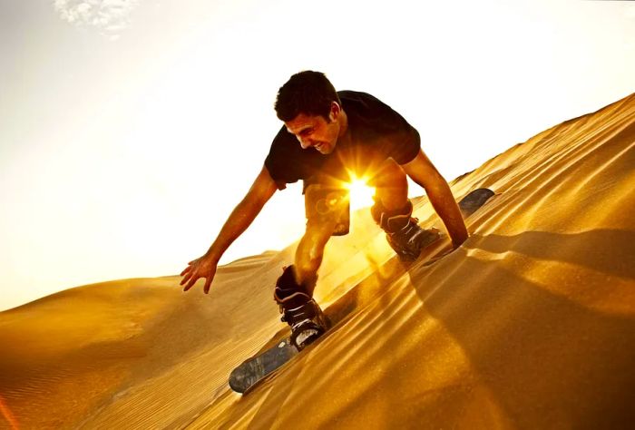 A man rides down the slope of the dunes on a sandboard.