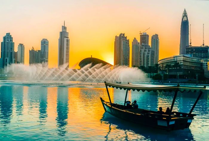 Visitors on a boat admire the fountain show against a backdrop of stylish skyscrapers under the twilight sky.