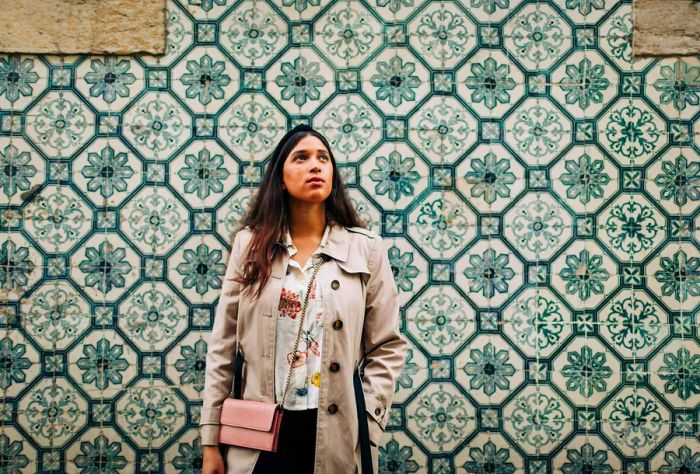 A stylish woman in casual attire poses next to a wall decorated with exquisite tiles.