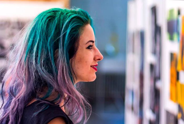 A woman with purple hair examines artworks on the wall.