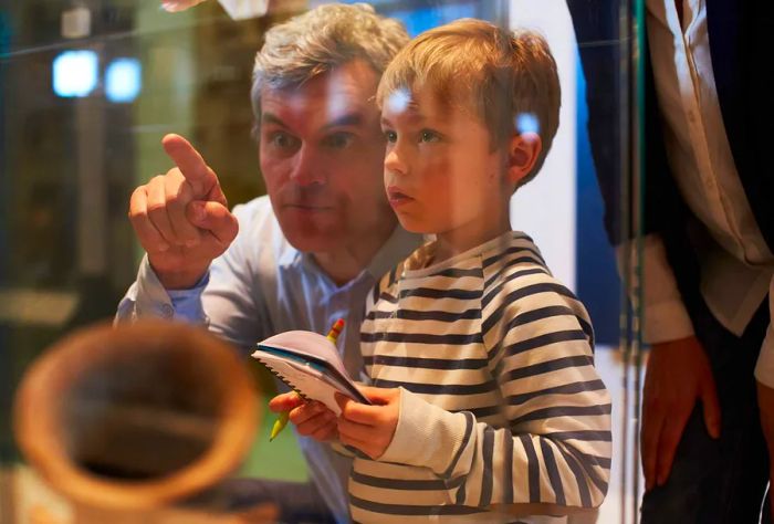 A father points at a display in a glass case while his son takes notes.