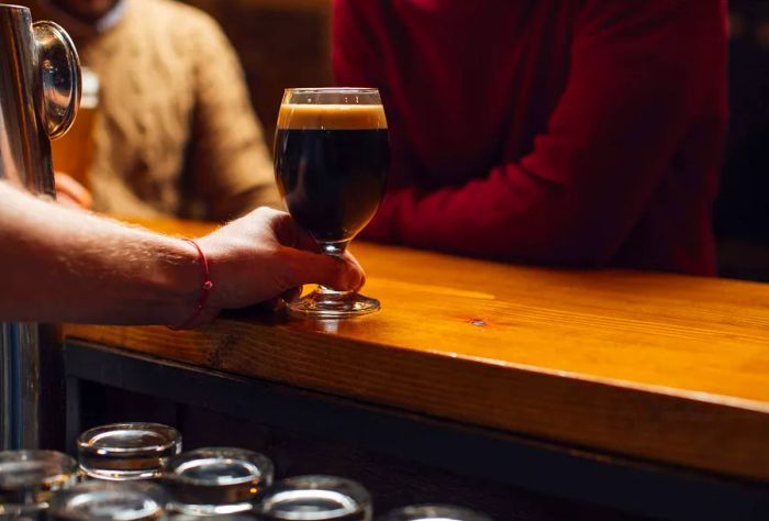 A bartender serves a glass of drink to patrons at the bar.