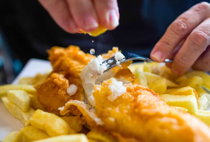 A man drizzling fresh lemon juice over his fish and chips.