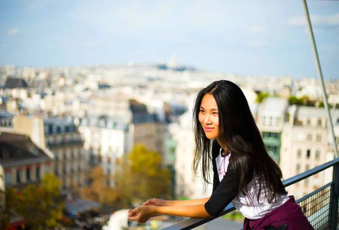 A woman with long hair beams while resting on a balcony at the Centre Pompidou, Paris, France