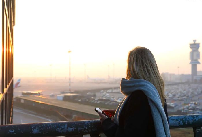 A woman gazes at the airport tarmac as the sun rises.