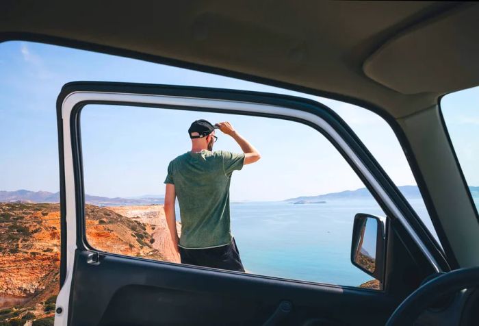 A man stands beside his parked car, door ajar, gazing out at the vast landscape before him.