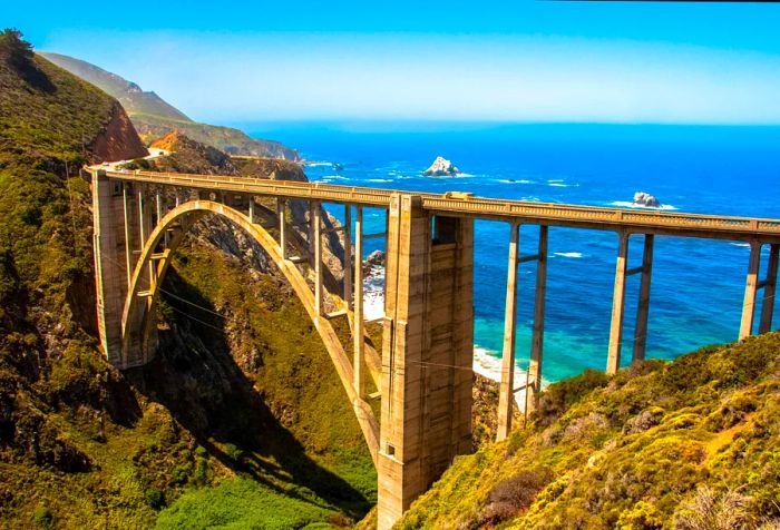 A towering arch bridge spanning a gorge between two cliffs, overlooking the ocean.