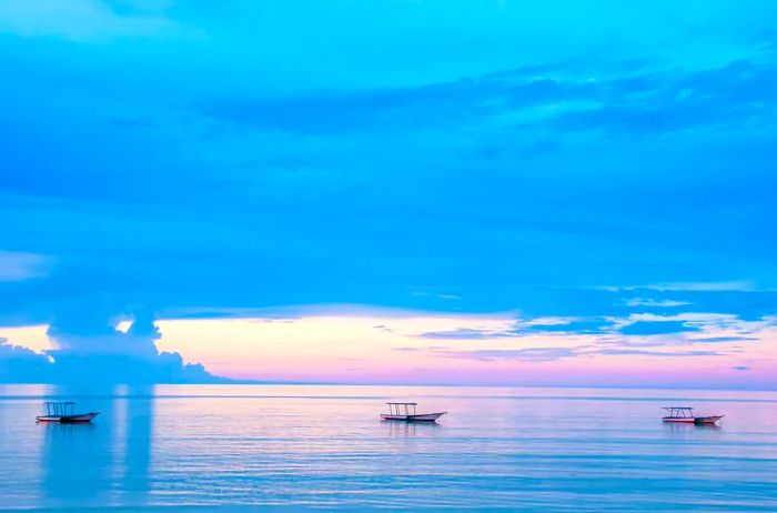 Vast ocean waters at sunset with three fishing boats, incredibly peaceful