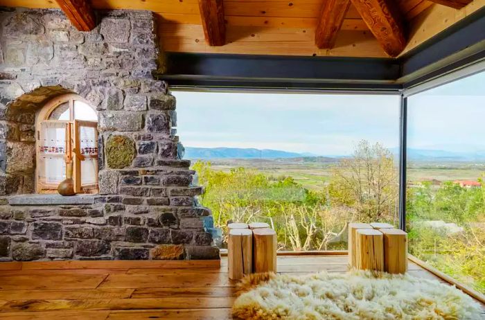 A hotel room with stone and glass walls offers stunning views of the countryside.