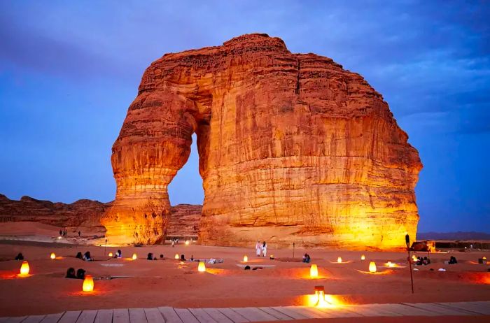 A panoramic view of the illuminated red sandstone monolith, known as Jabal Alfil, shaped over millions of years by wind and rain.