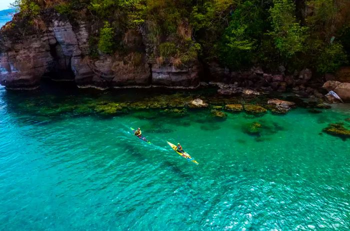 Two individuals paddle in the crystal-clear waters