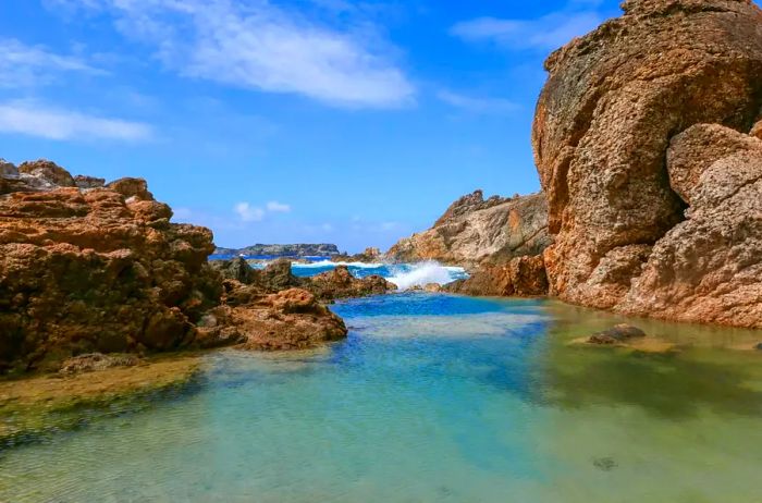 Waves crashing against verdant tidal pools along the rugged coastline of St. Barts