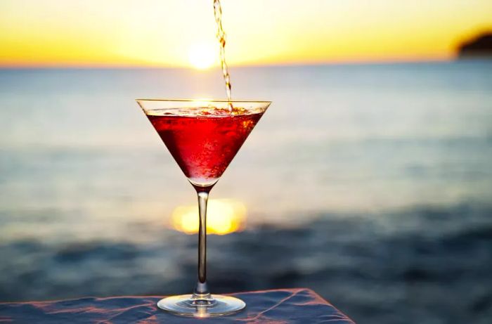 A cocktail being poured at a seaside table as the sun sets.