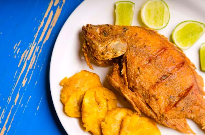 A plate featuring fried fish and plantains, garnished with lime slices.