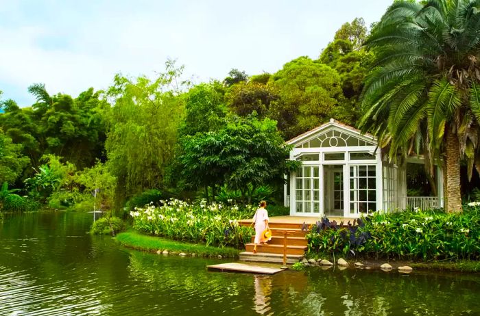 A greenhouse by the water's edge in a hotel garden, featuring a woman climbing the steps.