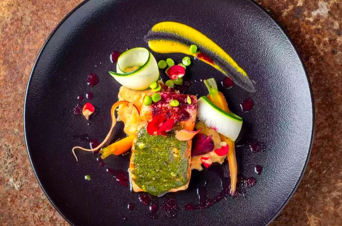 A plate of grilled salmon accompanied by fresh vegetables presented on a sleek black dish.