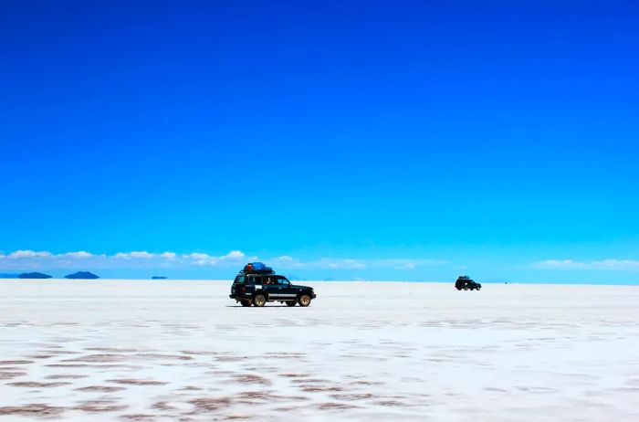 Black overland vehicles traversing the vast white salt flats of Bolivia.