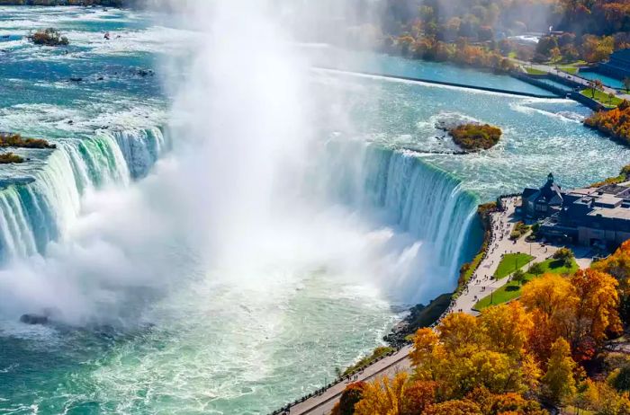 A view of the Niagara Falls Horseshoe Falls on a sunny autumn day, surrounded by colorful foliage in Niagara Falls City.