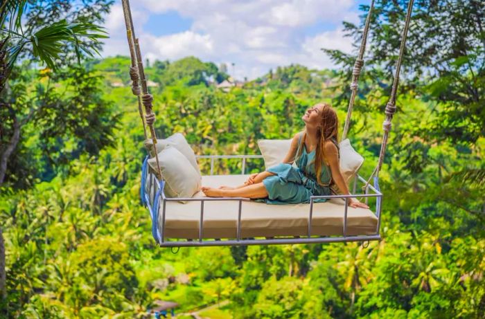 A young woman enjoying a swing amidst the lush rainforest of Bali, Indonesia. Experience the tropical swings—one of Bali's hottest trends.