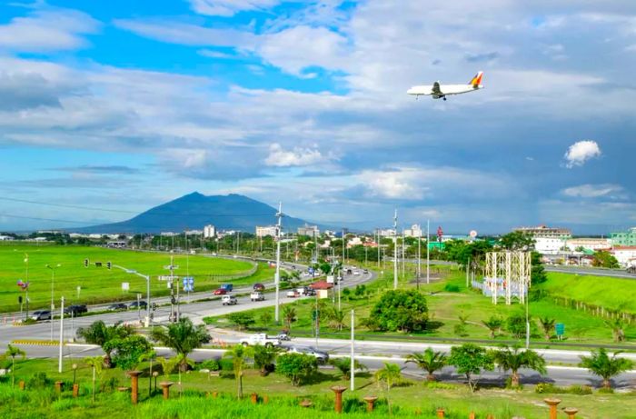 A Philippine Airlines Airbus A320 soars over a major road in the Clark Freeport Zone, preparing to land at Clark International Airport.